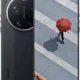 Black Xiaomi phone shown from rear and front; Leica camera module on back and screen displaying a person with a red umbrella on a striped plaza, with a long shadow.